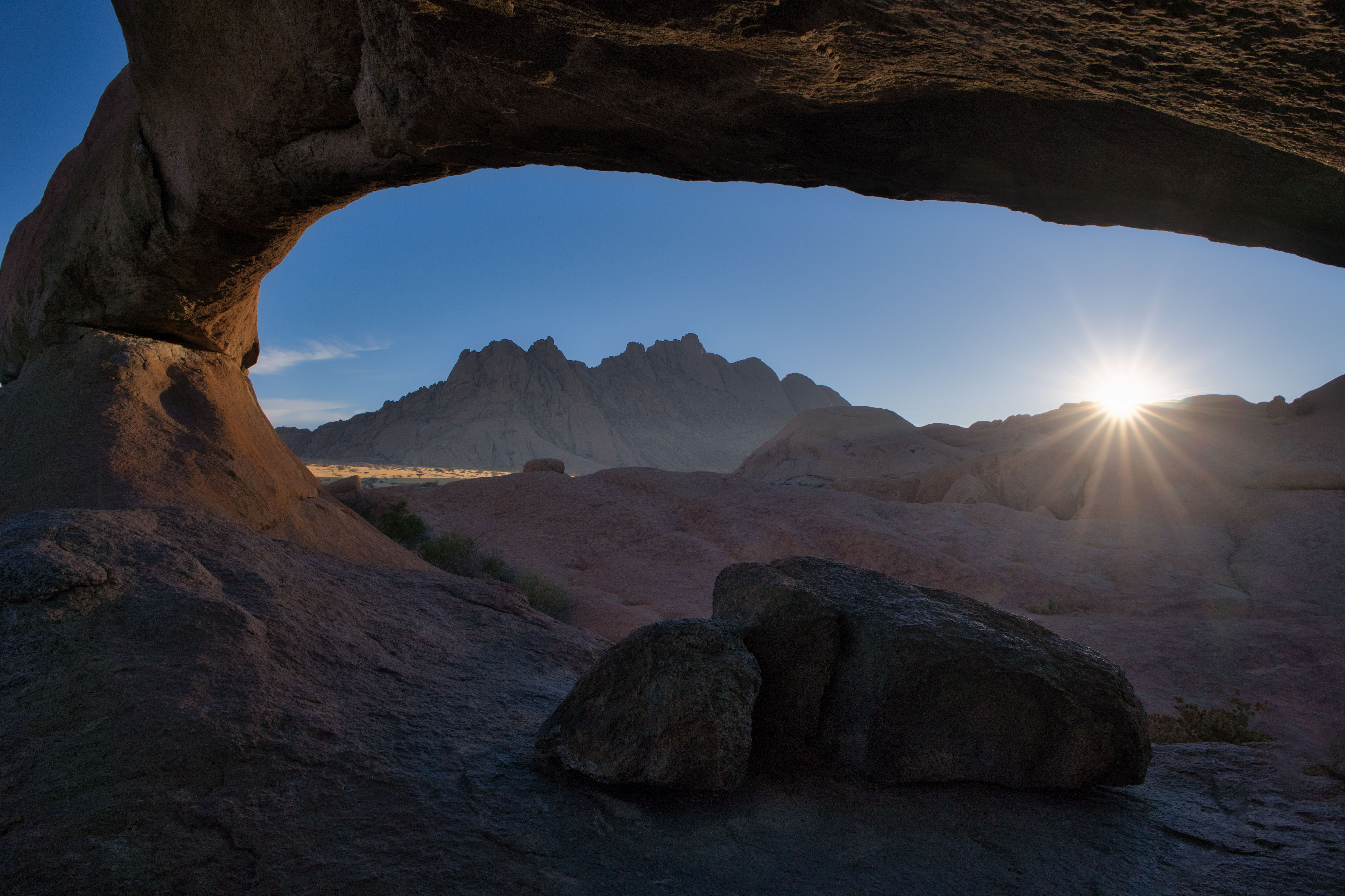 Arco de roca natural enmarcando montaña rocosa al atardecer en desierto de Namibia