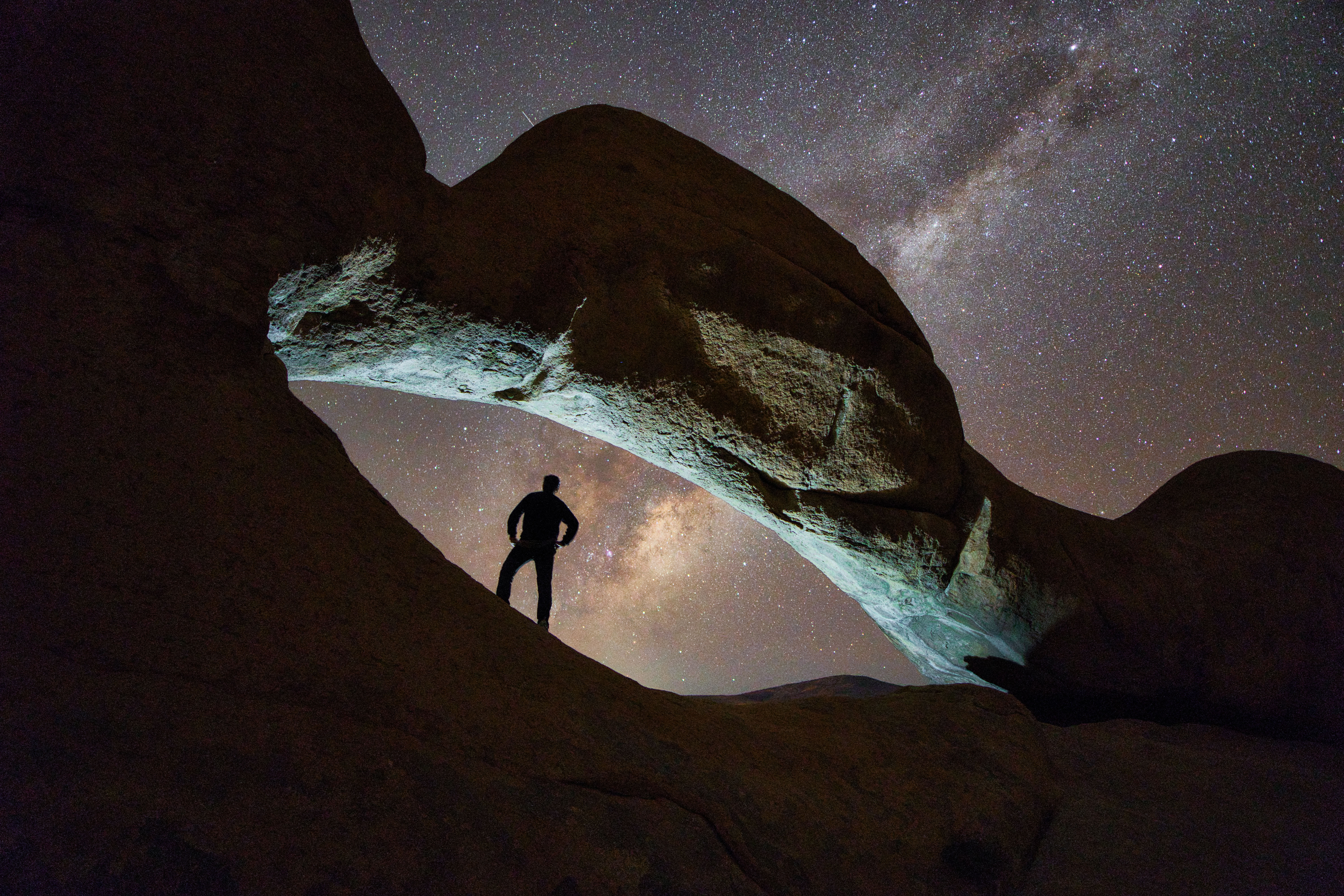 Viajero en silueta bajo formación rocosa natural con cielo estrellado y Vía Láctea visible en Namibia