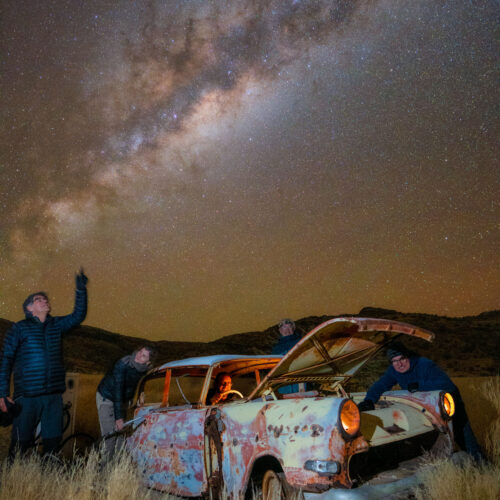 Grupo de viajeros junto a un vehículo abandonado bajo la Vía Láctea en el desierto de Namibia
