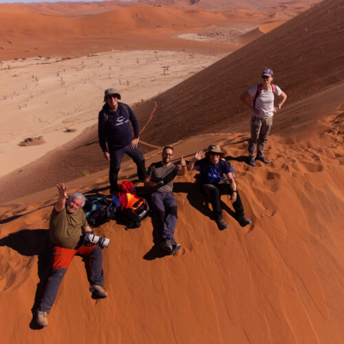 Grupo de expedicionarios posando en las dunas rojas de Namibia con vistas al valle desértico