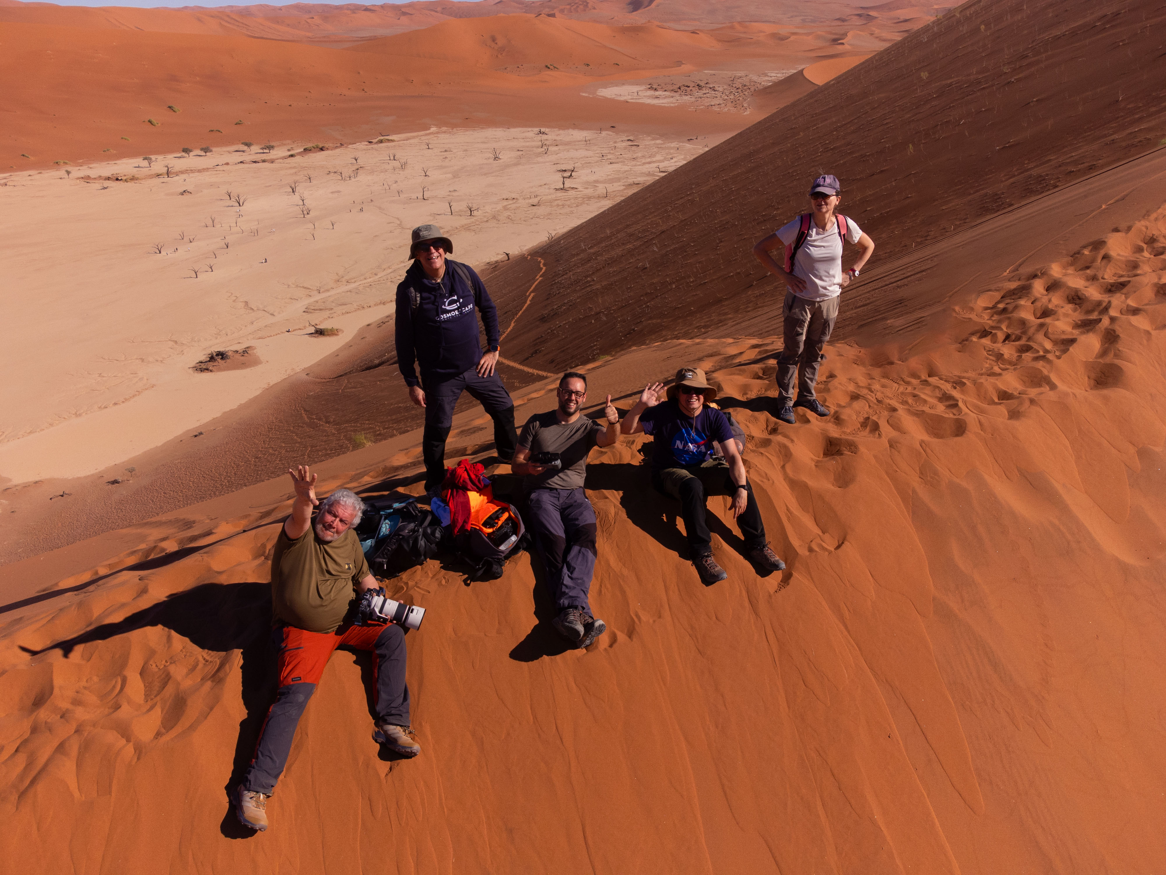Grupo de expedicionarios posando en las dunas rojas de Namibia con vistas al valle desértico