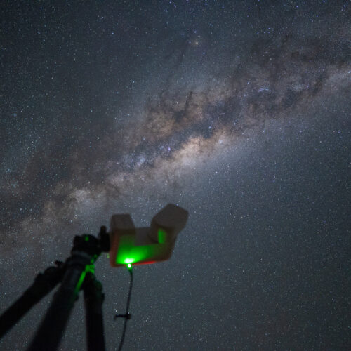 Telescopio con láser verde apuntando a la Vía Láctea en el cielo nocturno de Namibia