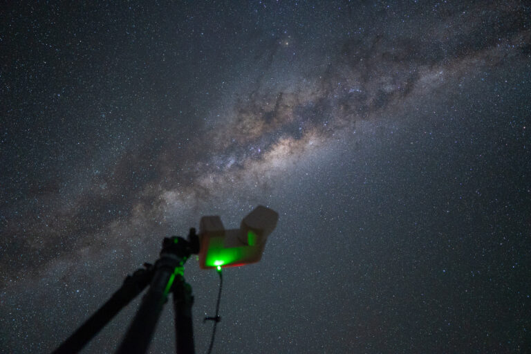 Telescopio con láser verde apuntando a la Vía Láctea en el cielo nocturno de Namibia