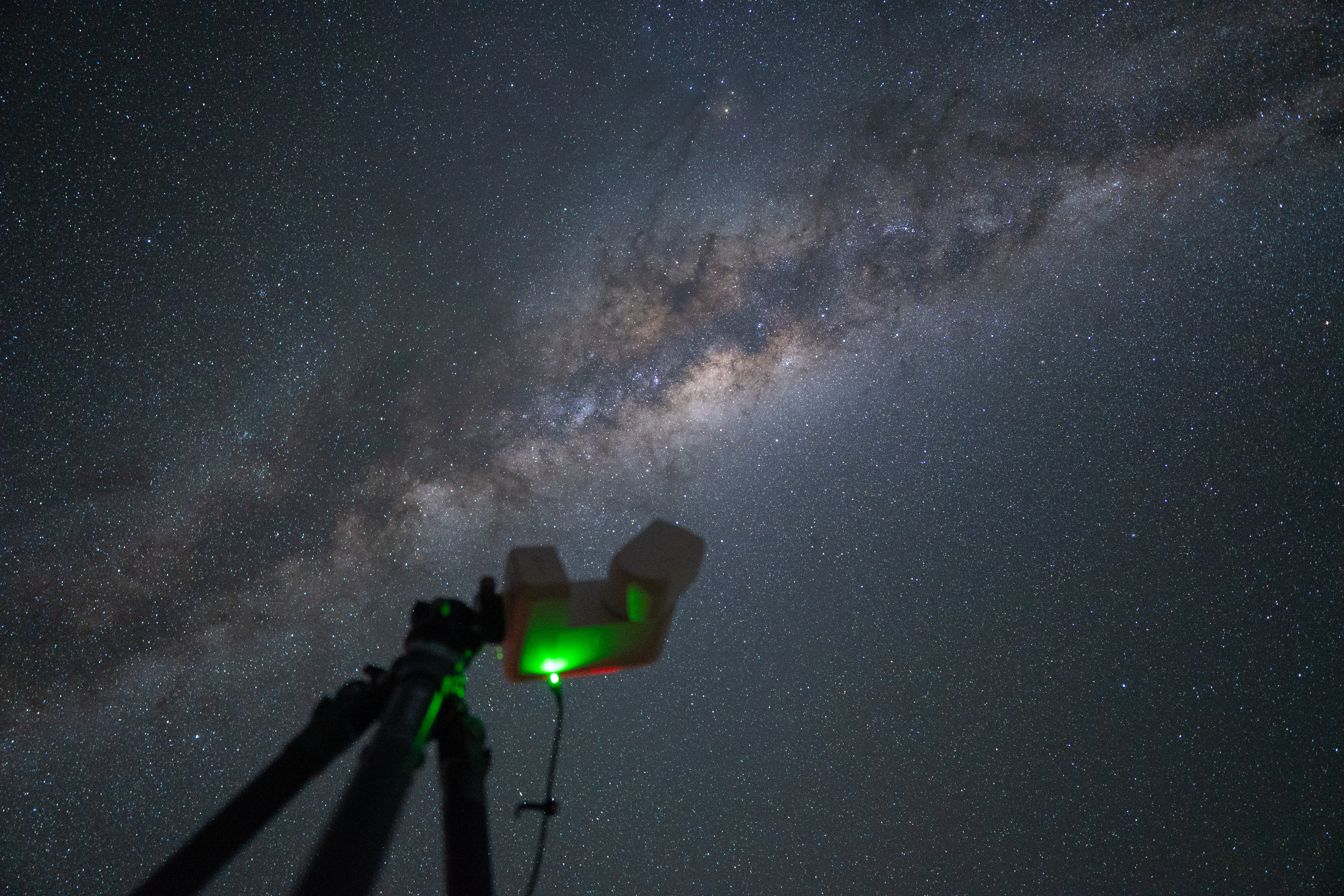 Telescopio con láser verde apuntando a la Vía Láctea en el cielo nocturno de Namibia