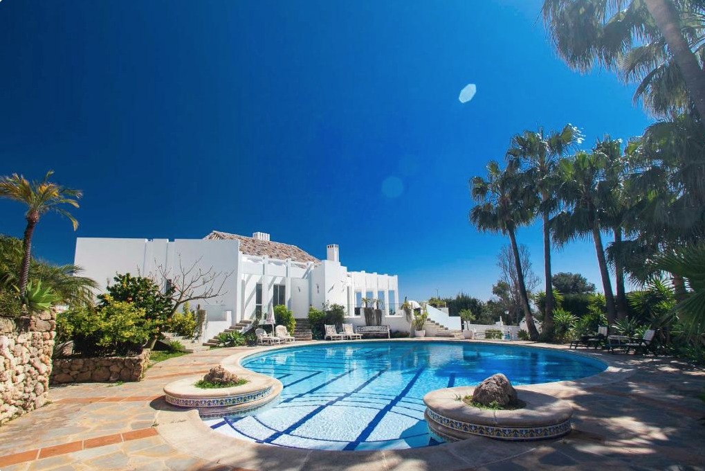 Villa blanca mediterránea con piscina olímpica azul, palmeras y cielo despejado