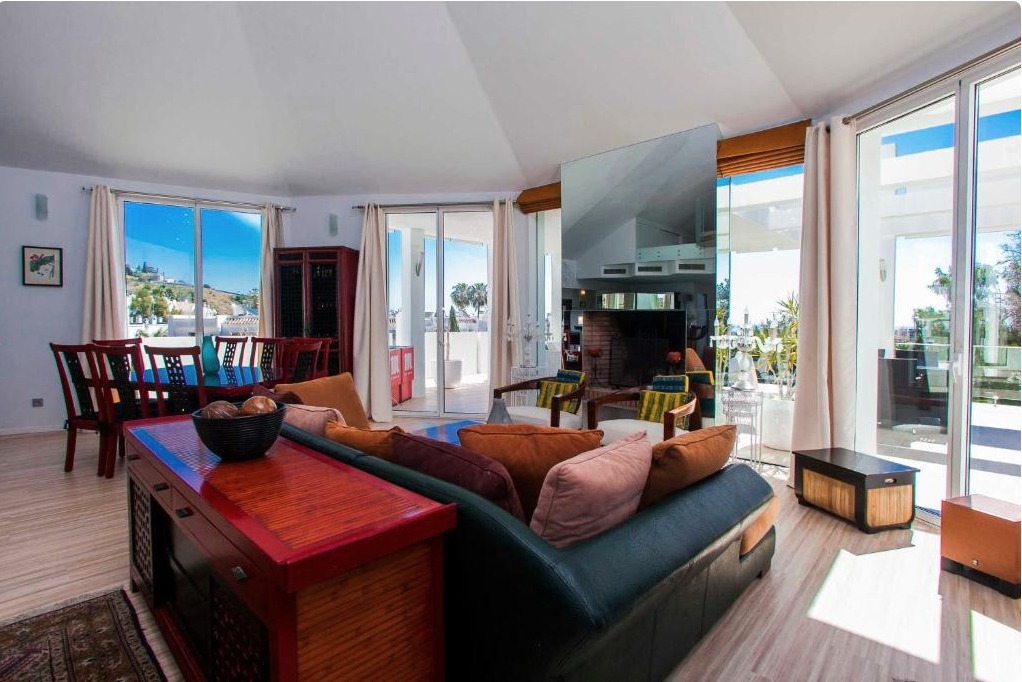 Luminoso salón de villa de lujo con sofá marrón, vista panorámica al mar Mediterráneo y terrazas acristaladas
