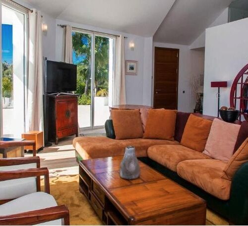 Sala de estar moderna con sofá naranja, sillones estampados, terraza con vistas al mar y decoración ecléctica en villa de lujo