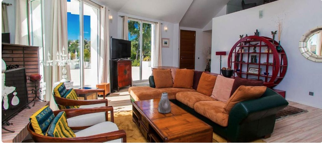 Sala de estar moderna con sofá naranja, sillones estampados, terraza con vistas al mar y decoración ecléctica en villa de lujo