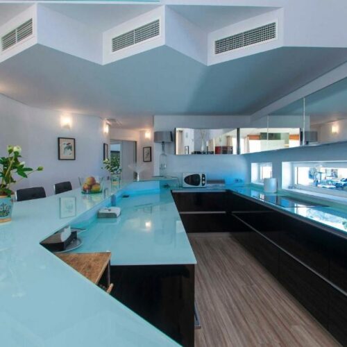 Cocina moderna de villa de lujo con isla central en tonos azules y negros, electrodomésticos premium y ventanales amplios.