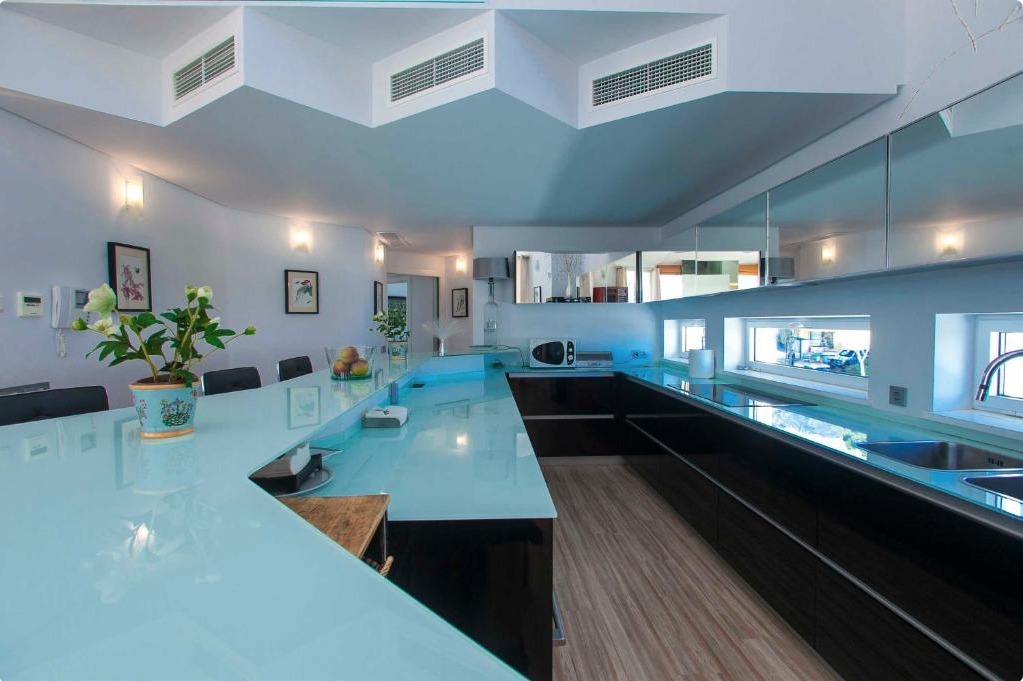 Cocina moderna de villa de lujo con isla central en tonos azules y negros, electrodomésticos premium y ventanales amplios.