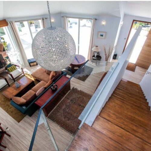Salón moderno de villa de lujo con vistas panorámicas, sofá naranja, lámpara de cristal colgante y escaleras de madera.
