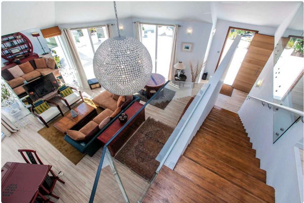 Salón moderno de villa de lujo con vistas panorámicas, sofá naranja, lámpara de cristal colgante y escaleras de madera.