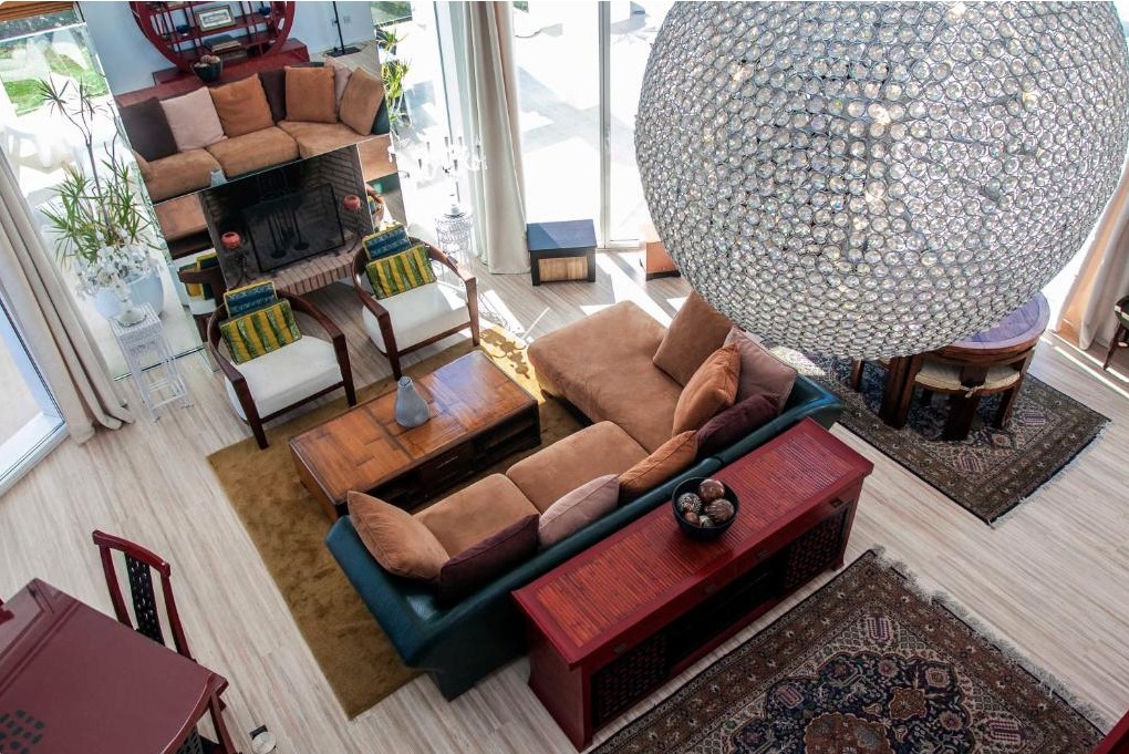 Salón moderno de villa de lujo con sofá terracota, lámpara de cristal, ventanales panorámicos y decoración eclética en tonos cálidos