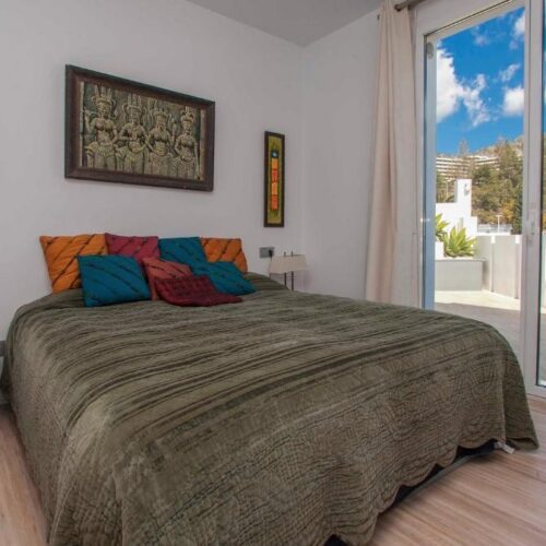 Dormitorio moderno con cama queen, almohadas de colores vibrantes, terraza con vistas a montañas y pueblo blanco andaluz