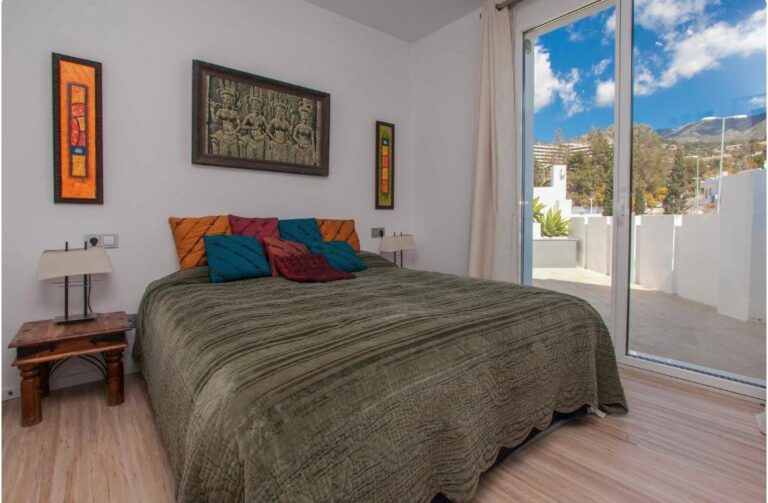 Dormitorio moderno con cama queen, almohadas de colores vibrantes, terraza con vistas a montañas y pueblo blanco andaluz