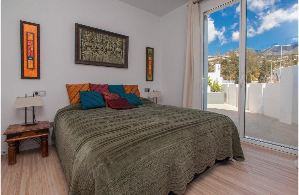 Dormitorio moderno con cama queen, almohadas de colores vibrantes, terraza con vistas a montañas y pueblo blanco andaluz