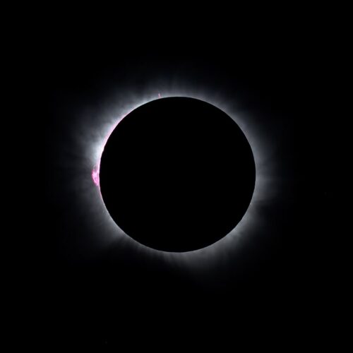 Eclipse solar total con corona solar visible y destello de protuberancia roja en el limbo lunar