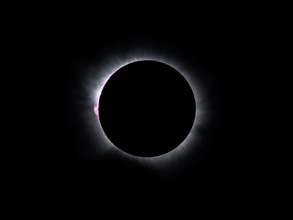 Eclipse solar total con corona solar visible y destello de protuberancia roja en el limbo lunar