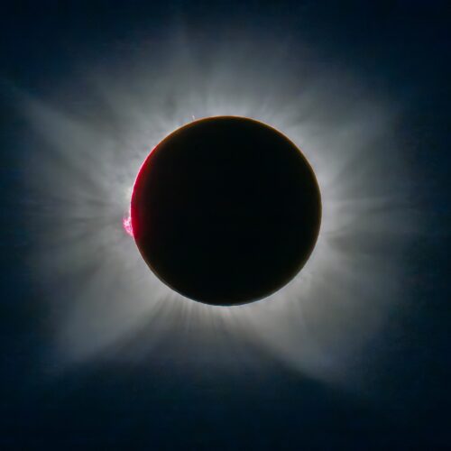 Eclipse solar total con corona visible, disco lunar negro cubriendo el sol y destello rojo en el borde