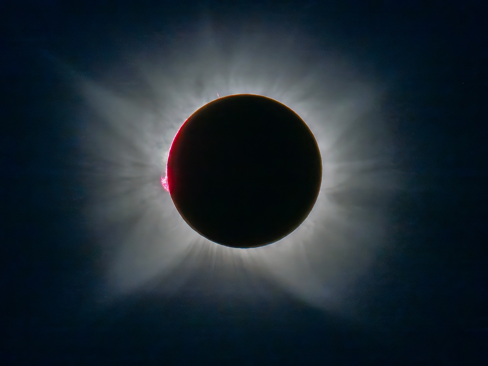 Eclipse solar total con corona visible, disco lunar negro cubriendo el sol y destello rojo en el borde