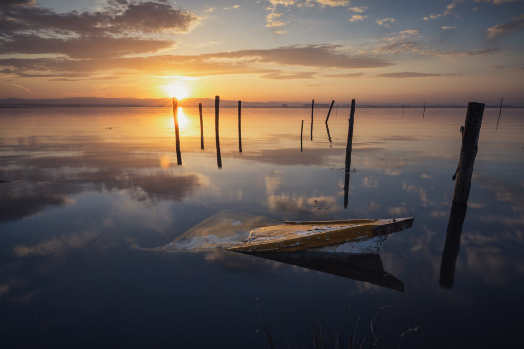 Barca de madera abandonada en aguas tranquilas al atardecer con postes de amarre reflejados