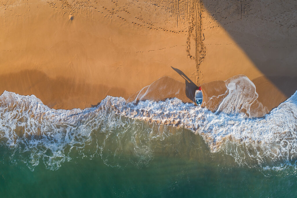 Surfista con tabla en la orilla del Algarve, visto desde arriba con arena dorada y olas turquesas