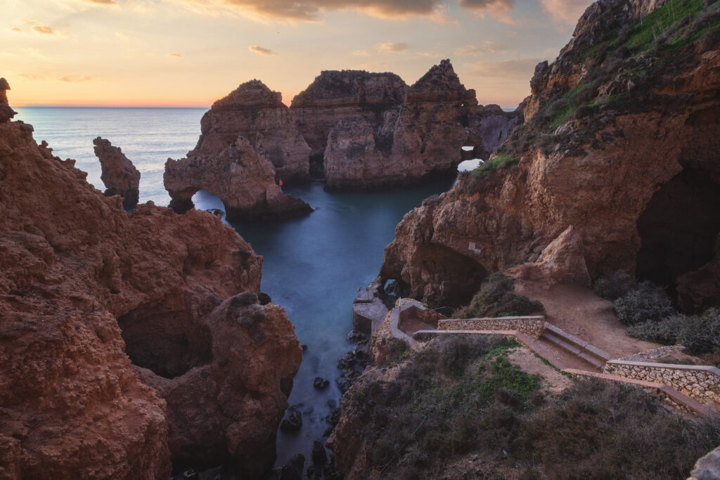 Acantilados rocosos de arenisca roja con calas turquesas al atardecer en el Algarve portugués