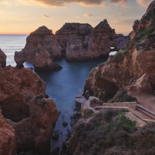 Acantilados rocosos de arenisca roja con calas turquesas al atardecer en el Algarve portugués