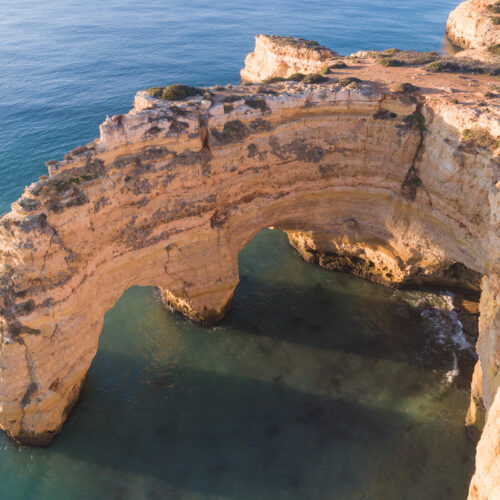 Arco de roca caliza en acantilado costero del Algarve bañado por agua azul