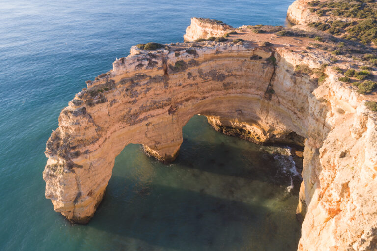 Arco de roca caliza en acantilado costero del Algarve bañado por agua azul
