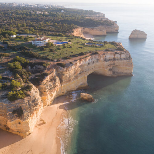 Acantilados de arenisca dorada con cueva marina y playa en el Algarve portugués, vegetación verde y mar turquesa al atardecer