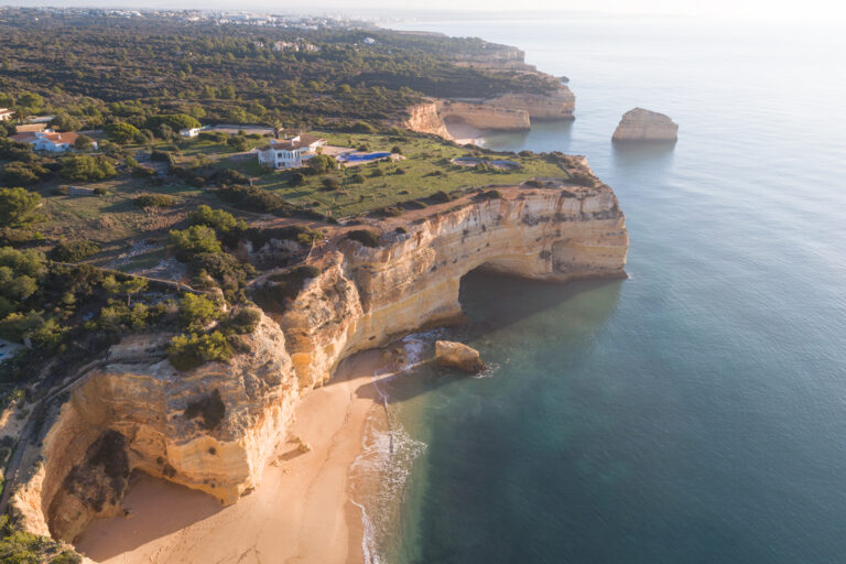 Acantilados de arenisca dorada con cueva marina y playa en el Algarve portugués, vegetación verde y mar turquesa al atardecer
