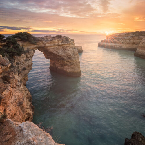 Arco de roca caliza en acantilado al atardecer sobre el mar turquesa del Algarve