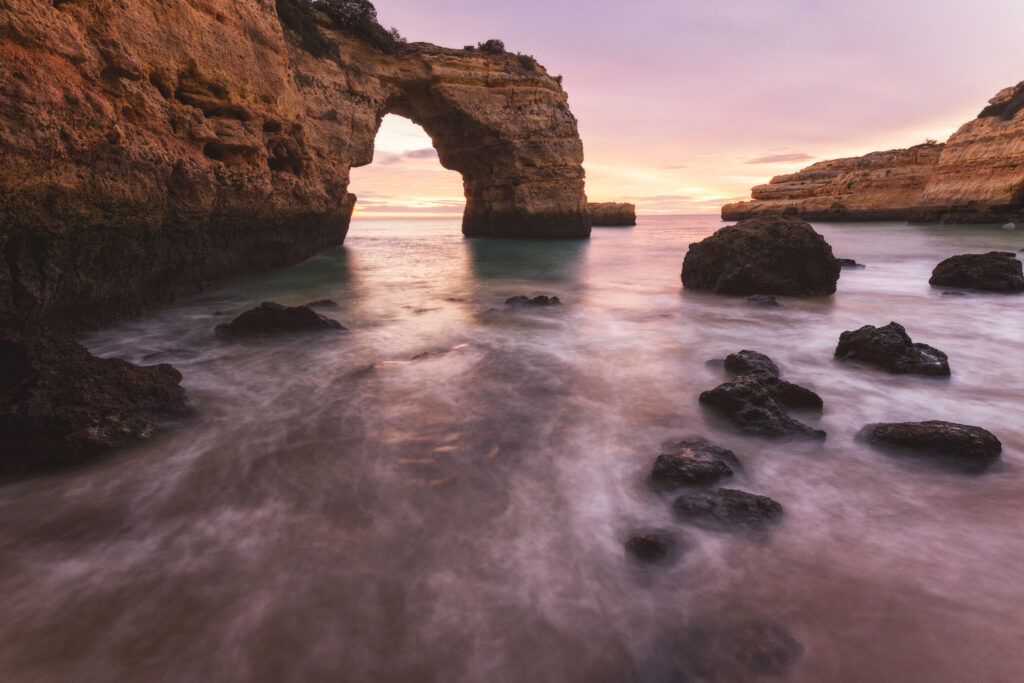 Arco de roca natural en acantilado costero al atardecer, rodeado de agua turquesa y rocas oscuras