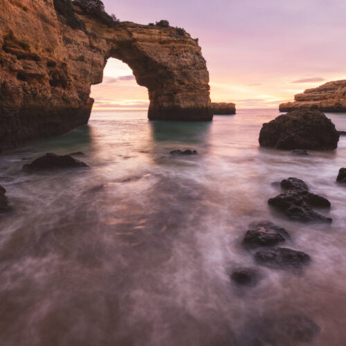 Arco de roca natural en acantilado costero al atardecer, rodeado de agua turquesa y rocas oscuras