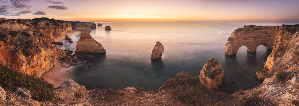 Acantilados rocosos del Algarve al atardecer con formaciones de piedra emergiendo del océano calmo
