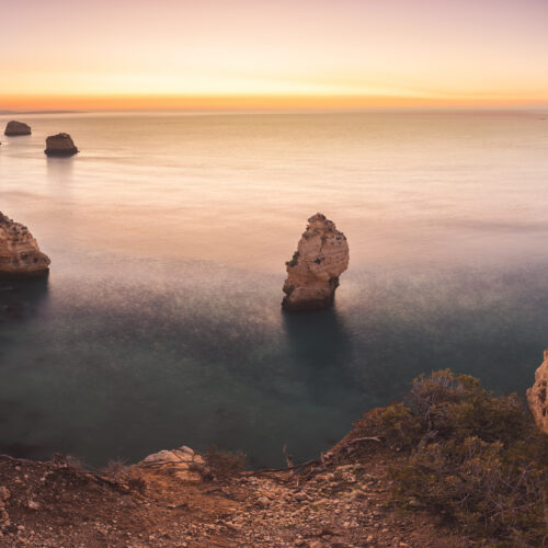 Acantilados rocosos del Algarve al atardecer con formaciones de piedra emergiendo del océano calmo