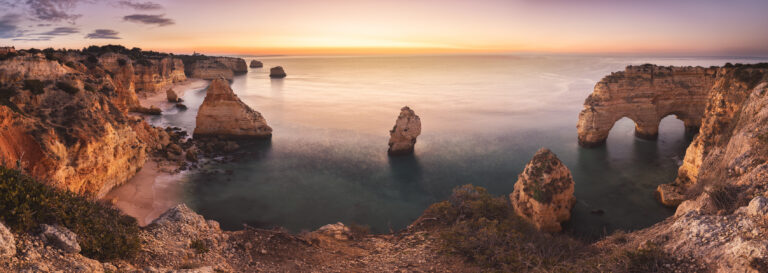 Acantilados rocosos del Algarve al atardecer con formaciones de piedra emergiendo del océano calmo