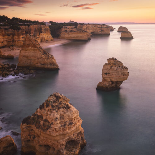 Acantilados rocosos al atardecer en el Algarve, con formaciones de piedra emergiendo del mar en calma
