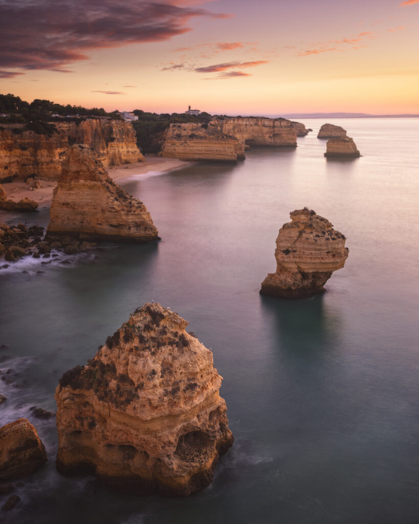 Acantilados rocosos al atardecer en el Algarve, con formaciones de piedra emergiendo del mar en calma