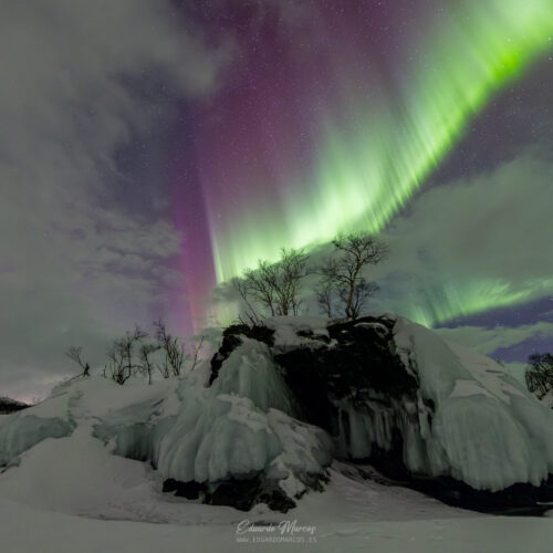 Aurora boreal verde y púrpura sobre roca congelada cubierta de hielo en paisaje nevado de Abisko
