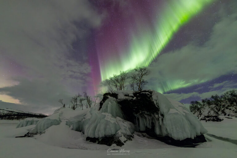 Aurora boreal verde y púrpura sobre roca congelada cubierta de hielo en paisaje nevado de Abisko