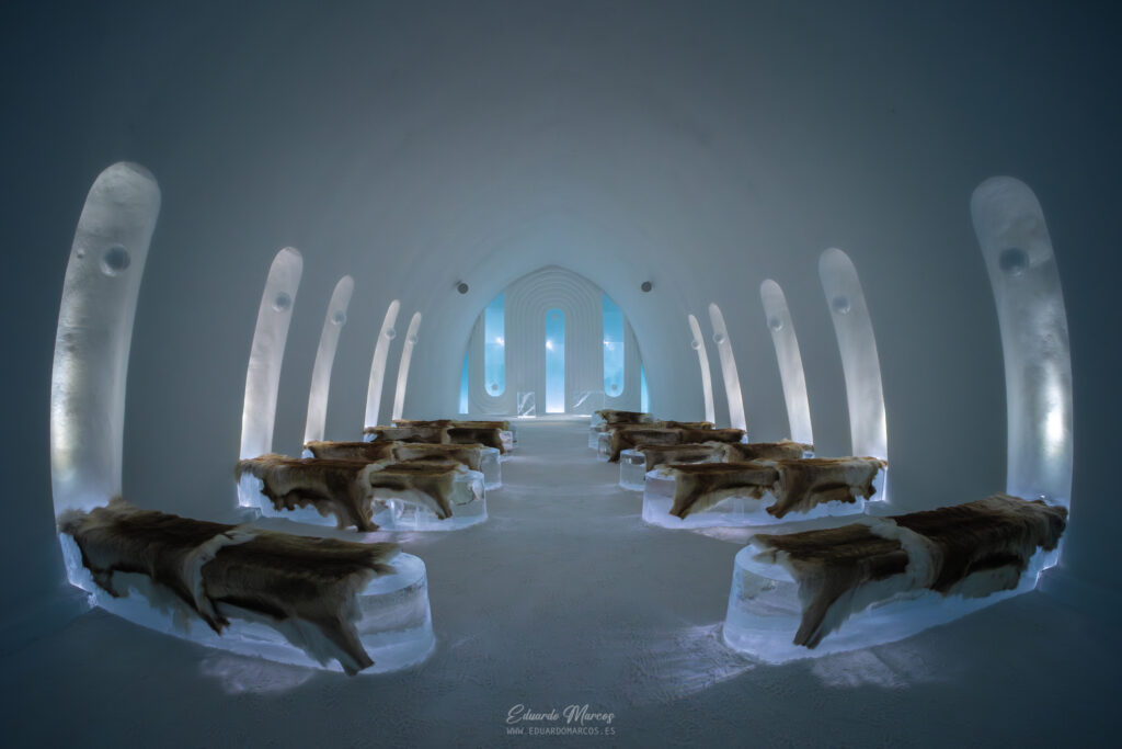 Interior de iglú de hielo en Abisko con troncos de madera y luz azul natural filtrándose por ventanas arqueadas