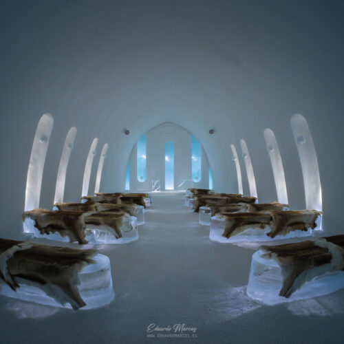Interior de iglú de hielo en Abisko con troncos de madera y luz azul natural filtrándose por ventanas arqueadas