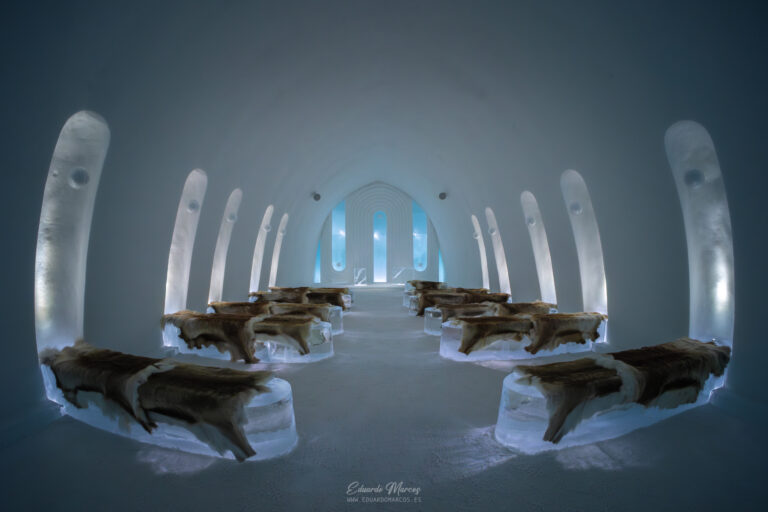 Interior de iglú de hielo en Abisko con troncos de madera y luz azul natural filtrándose por ventanas arqueadas