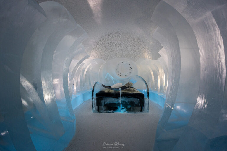 Interior de túnel de hielo azul con estructura de hielo en las paredes y zona de descanso con equipamiento negro al fondo