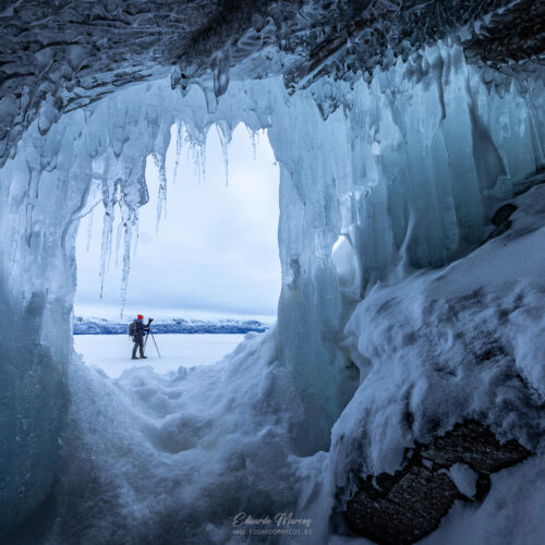 Aventurero dentro de una cueva de hielo frente a un lago congelado en Abisko, Suecia