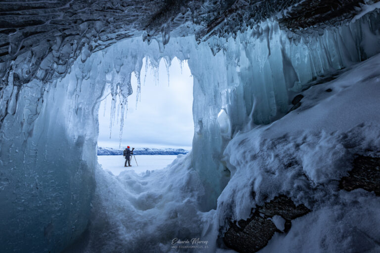 Aventurero dentro de una cueva de hielo frente a un lago congelado en Abisko, Suecia
