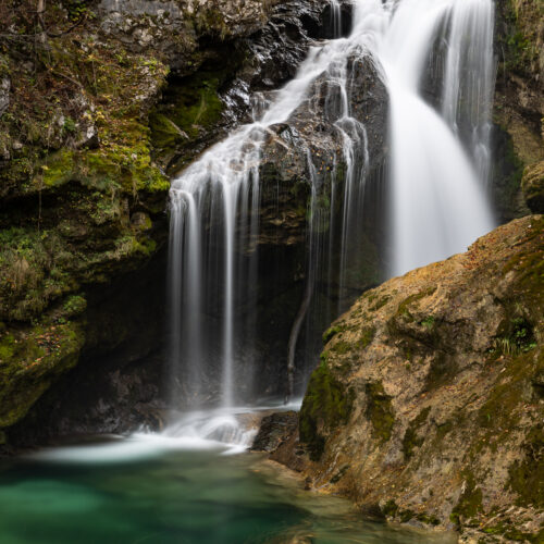 Cascada de aguas blancas en garganta rocosa con piscina turquesa rodeada de musgo y vegetación