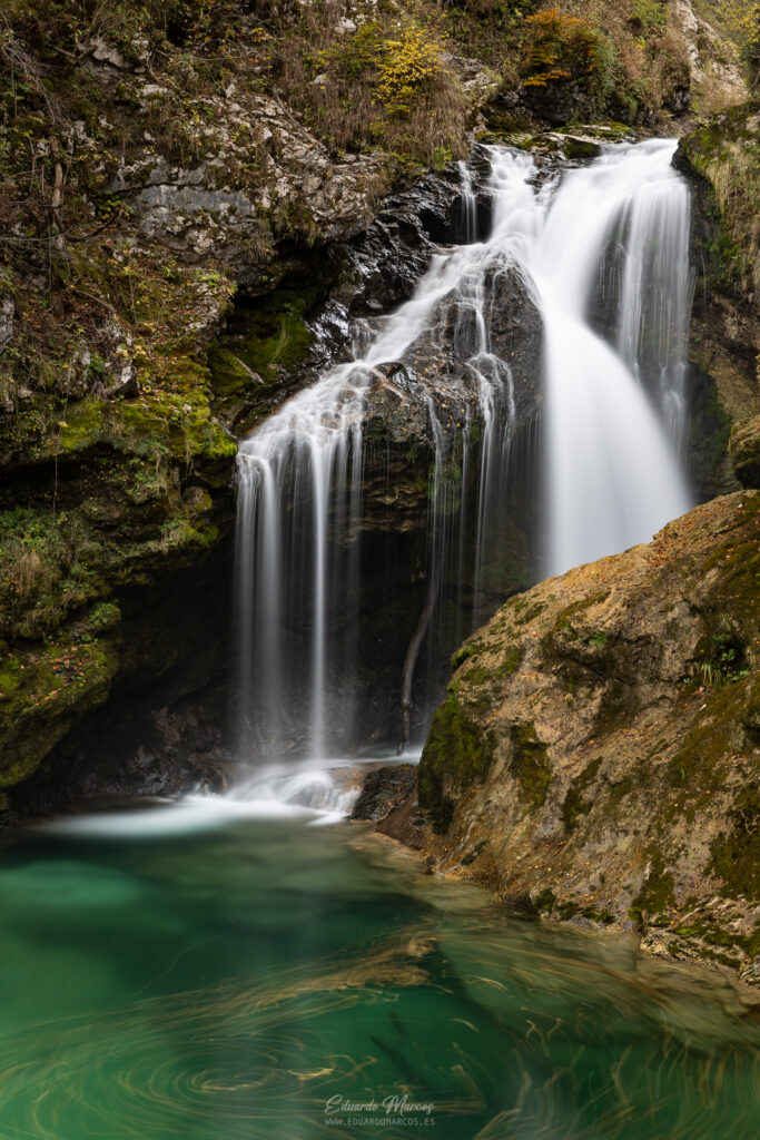Cascada de aguas blancas en garganta rocosa con piscina turquesa rodeada de musgo y vegetación